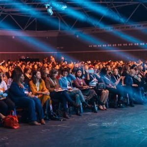 Vibrant image of a diverse audience seated in a large auditorium, highlighted by dynamic stage lighting.